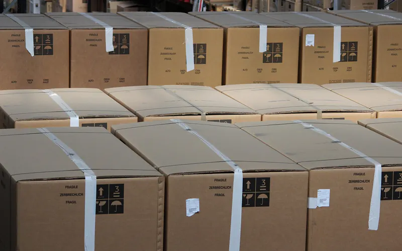 Rows of taped cardboard shipping cartons marked with handling symbols, staged in a warehouse