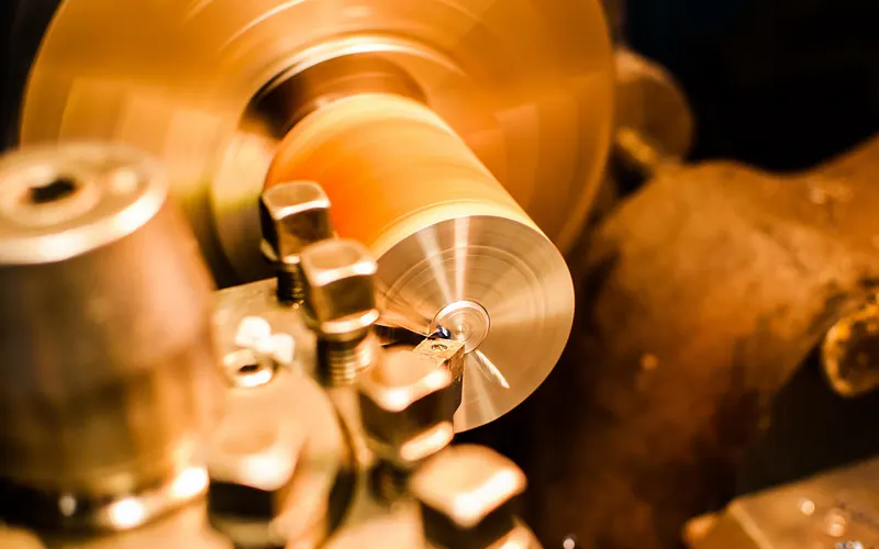 Close-up of a lathe turning a brass part, with the cutting tool against the spinning workpiece